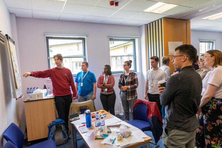 The Data Lab Academy Msc students participating in Innovation Week. 6 people looking at a whiteboard. They look to be solving a complex problem.