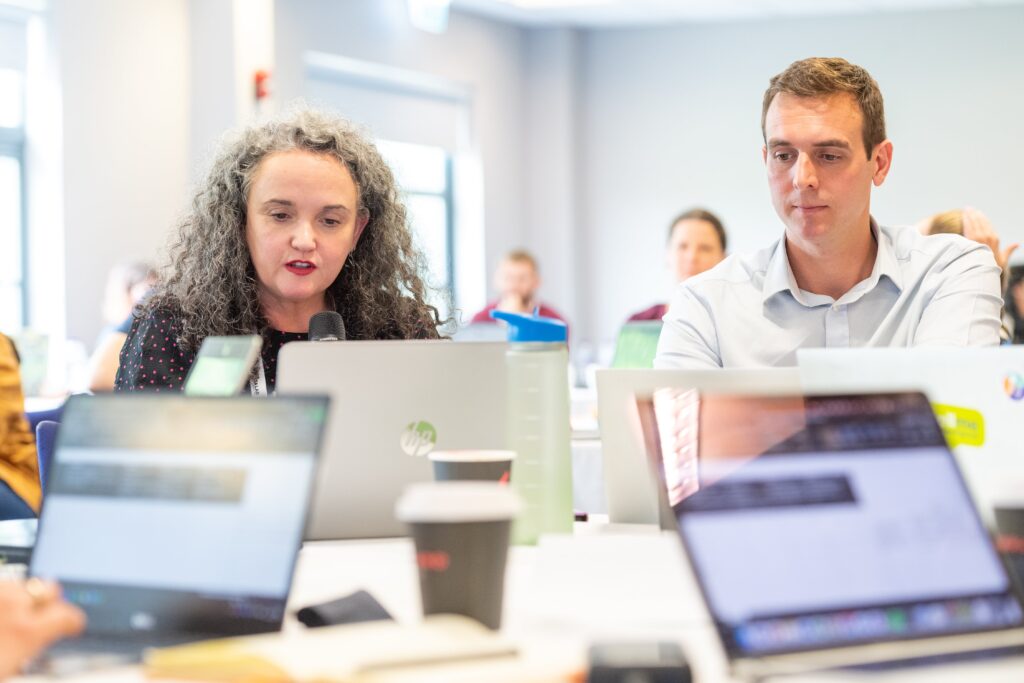 Focus on two people sitting around a crowded table where people are working on their laptops