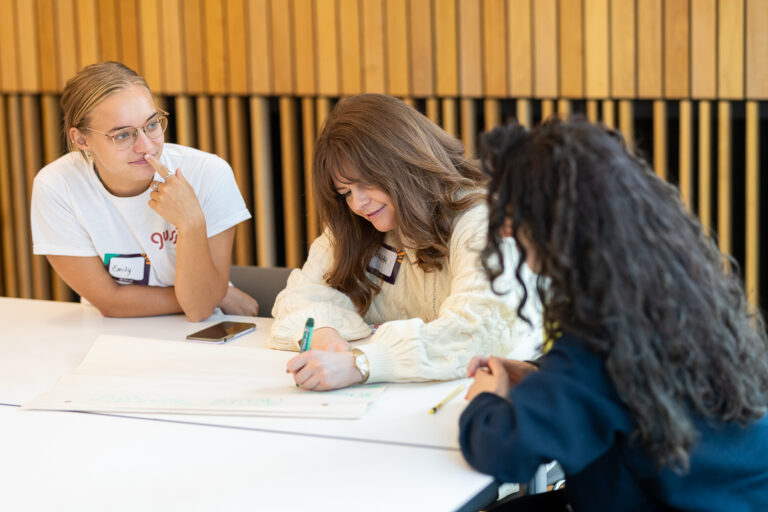 three people smiling and working together, filling a piece of paper.