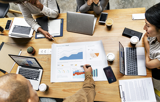 Business people sitting round table with charts and laptops