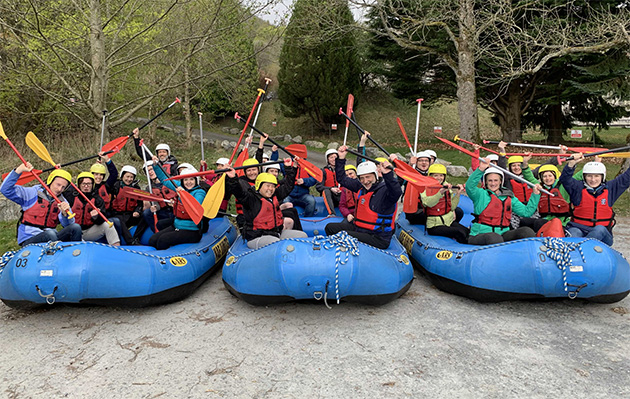 The Data Lab team photo in 3 river rafting boats, wearing helmets, waving paddles