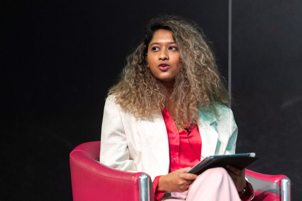 Photo of Tricia Govindasamy seated and speaking on stage at a conference.