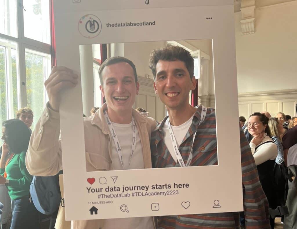 two students smiling thrown a cardboard instagram frame
