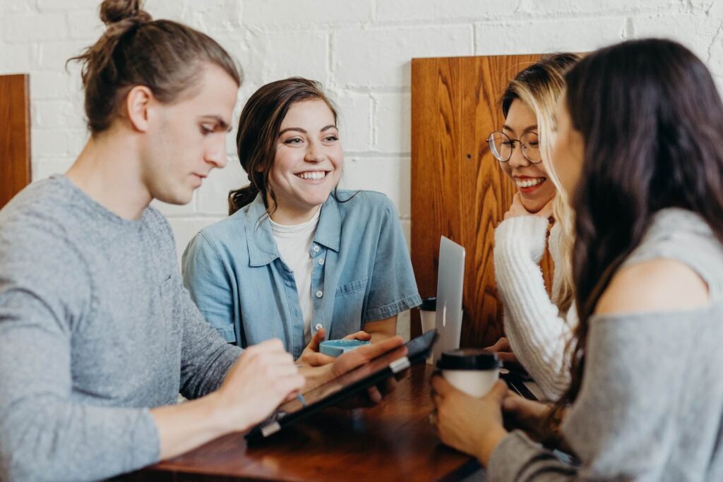 4 people sat smiling around a table with laptops and ipads
