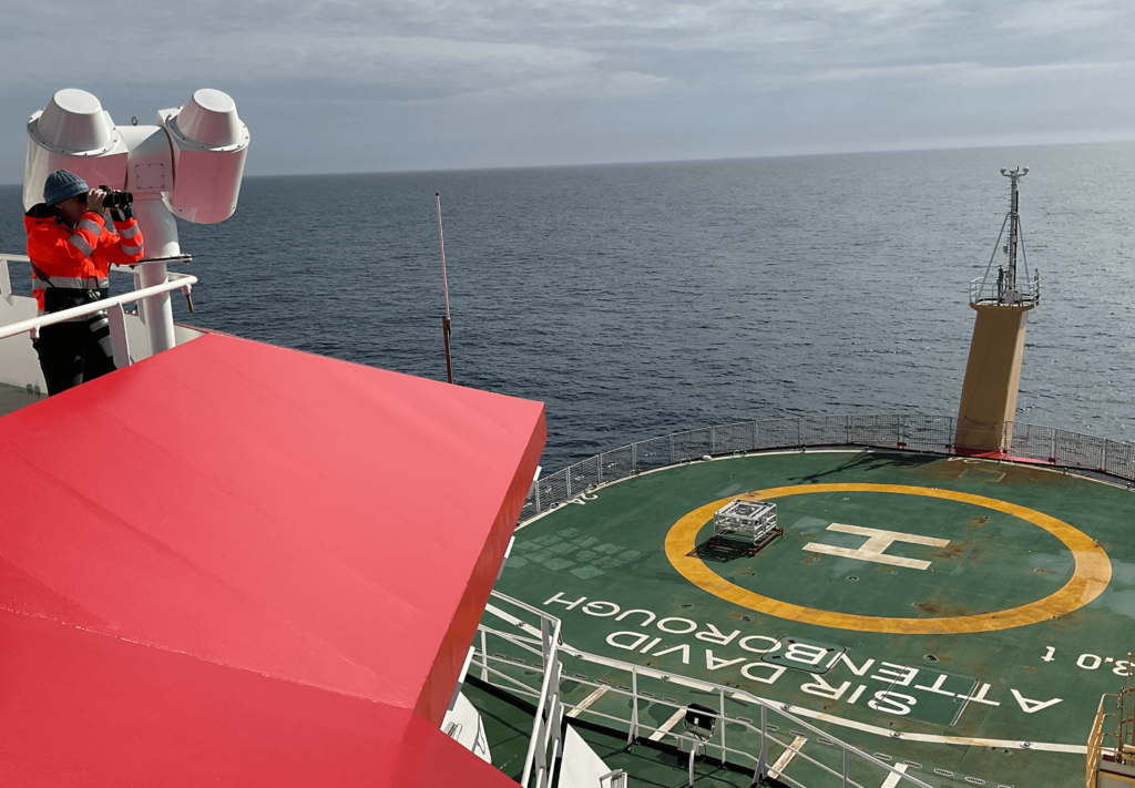 person on an aircraft carrier looking through binoculars out to see