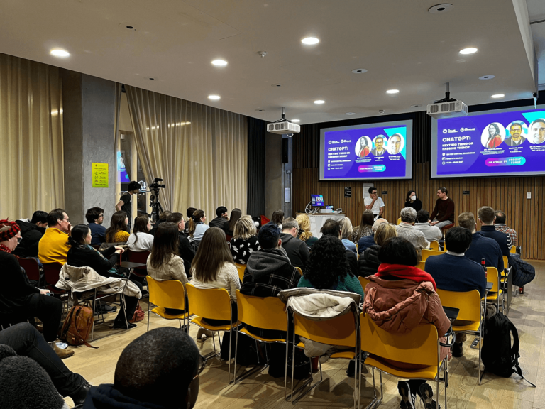 The Data Lab Chat GPT panel event - a room of people listening to a talk with the panelist images shown on screens above them